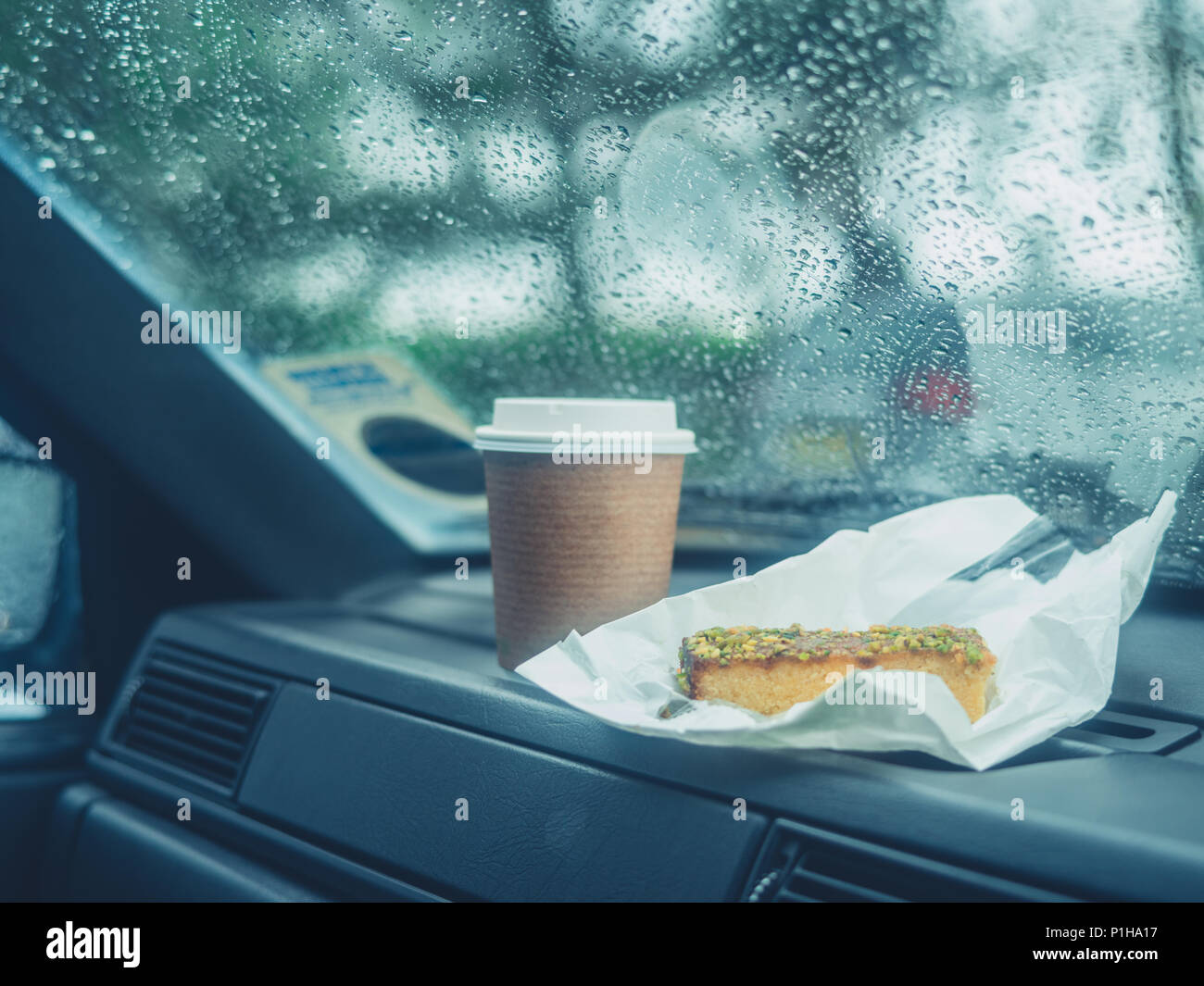 Un tasse de café et une tranche de gâteau sur le bord d'une voiture un jour de pluie Banque D'Images