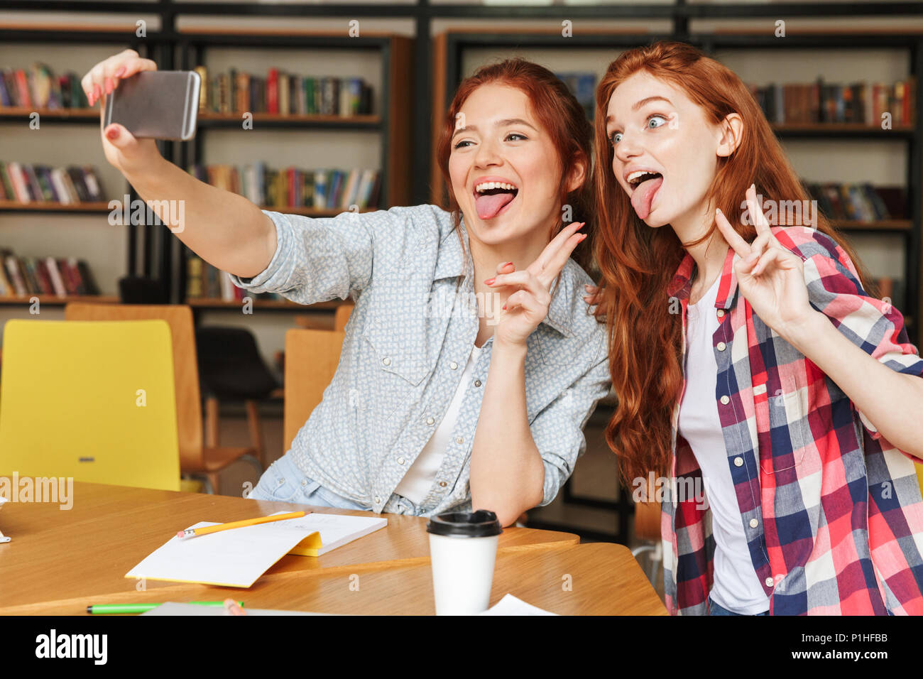 Portrait d'un drôle de prendre deux adolescentes selfies avec téléphone mobile tout en restant assis à la bibliothèque Banque D'Images