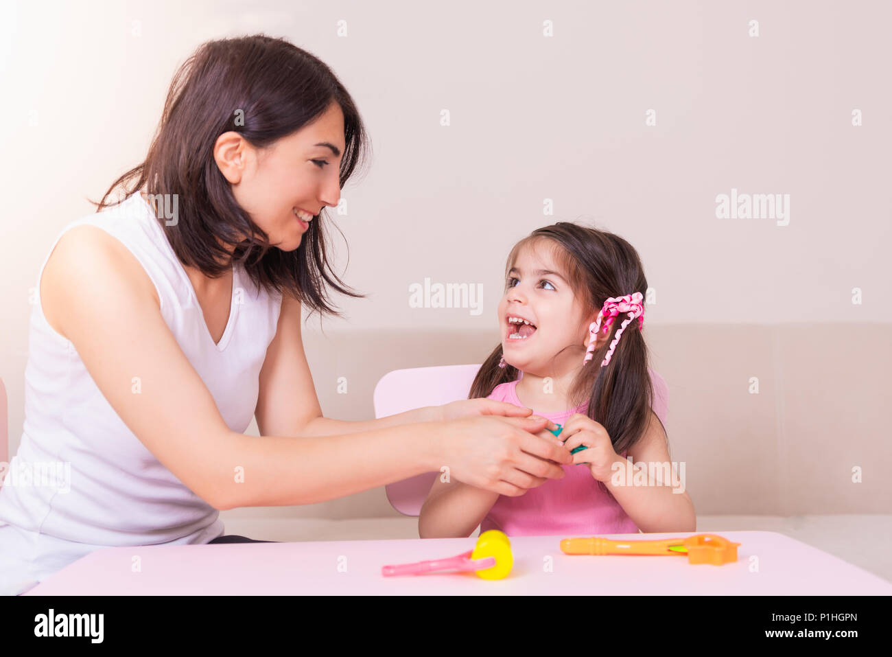Heureux belle mère et fille mignonne à jouer ensemble avec de la pâte à modeler tout en restant assis sur table. Banque D'Images