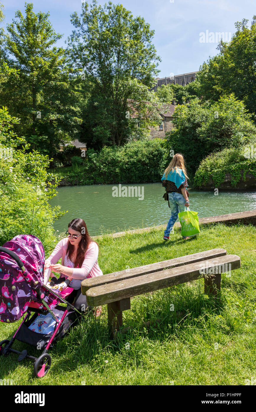 Une jeune femme s'occupe d'un bébé dans un pushcharir, un autre porte un sac shopping dans la zone de pique-nique par la rivière Avon Tetbury, Malmesbury, Wiltshire, Royaume-Uni Banque D'Images