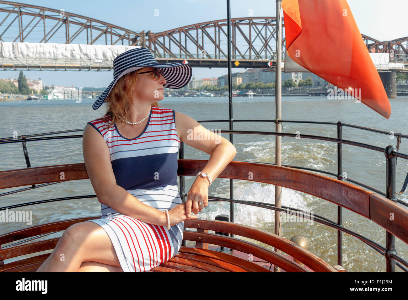 Un joli sourire femme élégante dans un chapeau, âge moyen, assis sur un banc de ferry, bénéficiant d'une promenade touristique. Un petit traversier sur la rivière Vltava dans le Banque D'Images