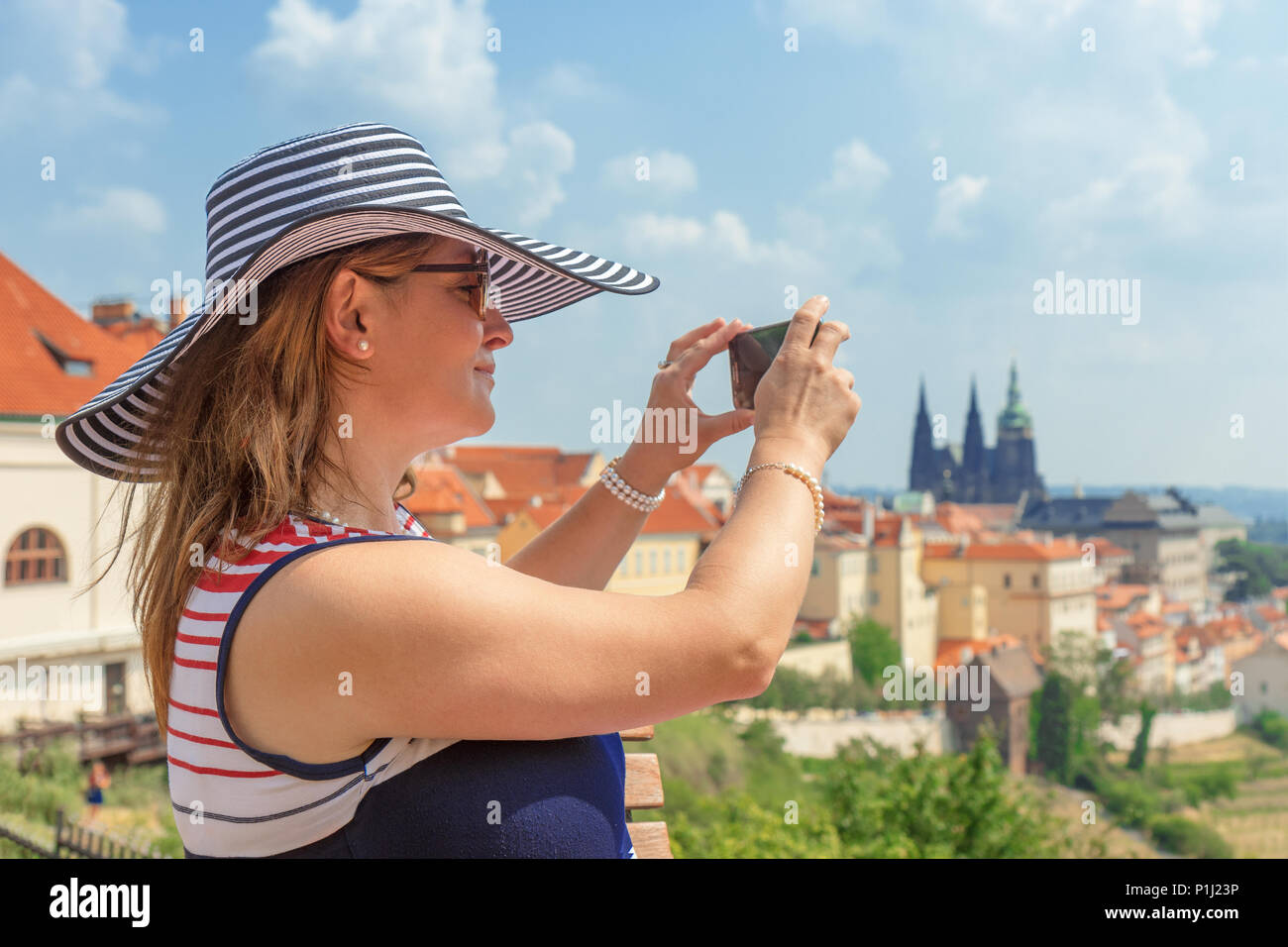 Un joli sourire femme élégante dans un chapeau, âge moyen, assis sur une terrasse d'observation du monastère de Strahov et prendre des photos d'un beau panorama de Banque D'Images