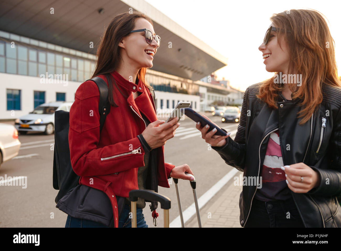 Photo de deux excités femmes européennes qui voyagent à l'étranger et l'utilisation de téléphones mobiles lors de l'attente pour le vol ou après le départ debout avec assurance près de ai Banque D'Images