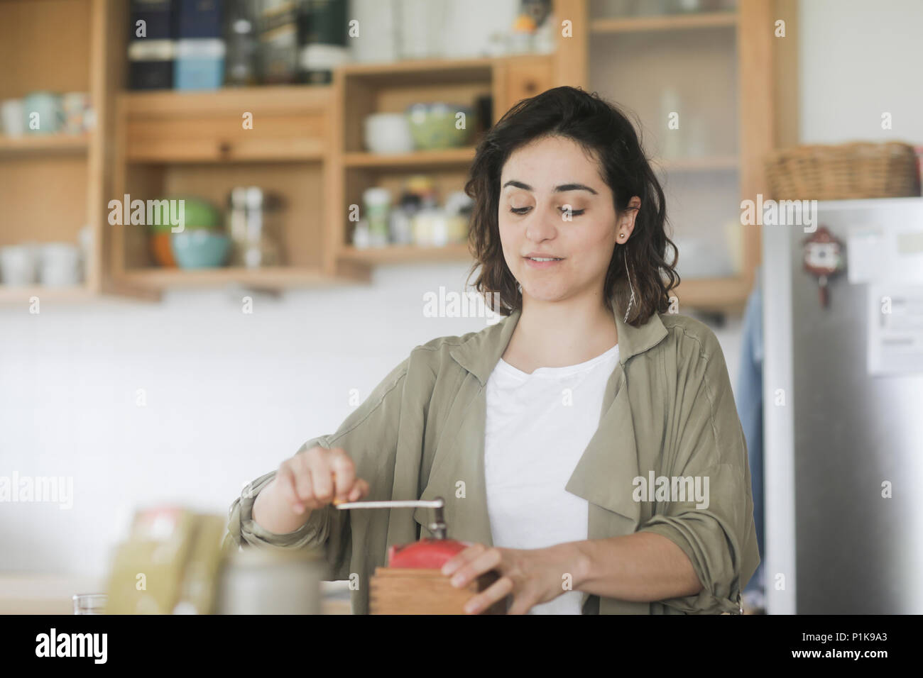 Femme debout dans la cuisine à l'aide d'un vieux moulin à café Banque D'Images