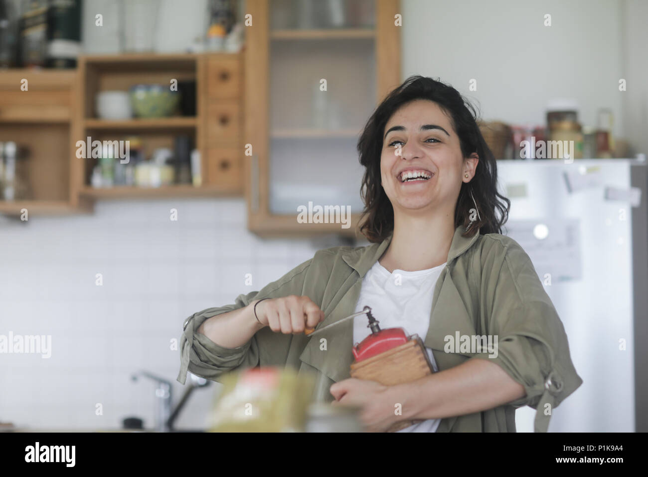 Smiling Woman standing dans la cuisine à l'aide d'un vieux moulin à café Banque D'Images