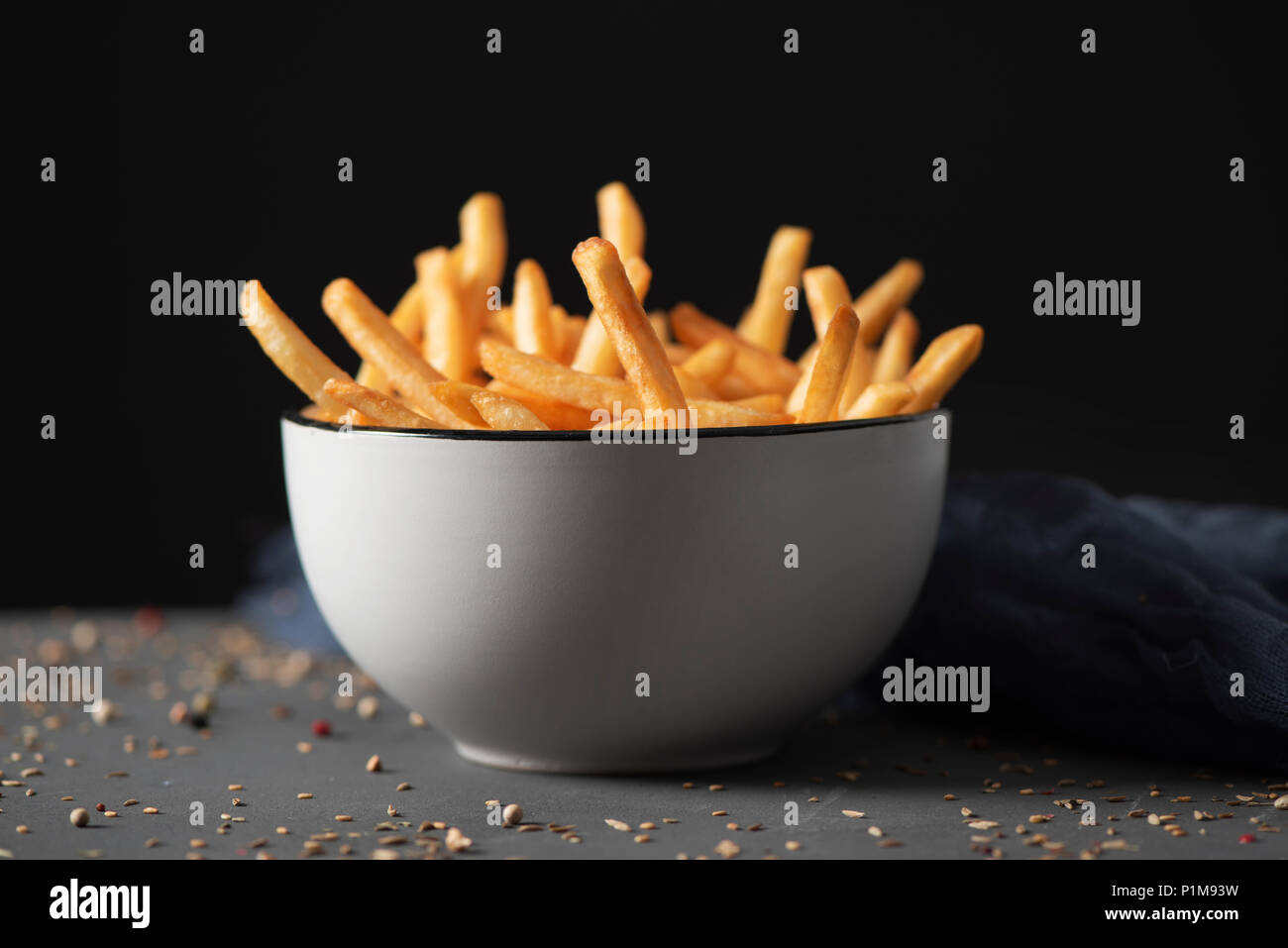 Quelques frites appétissant servi dans un bol en céramique blanc, placé sur une table en bois rustique gris, sur un fond noir Banque D'Images