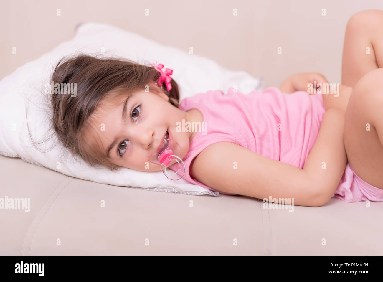 Portrait of cute girl lying on a bed avec sucette dans sa bouche. Focus sélectif et petite profondeur de champ. Banque D'Images