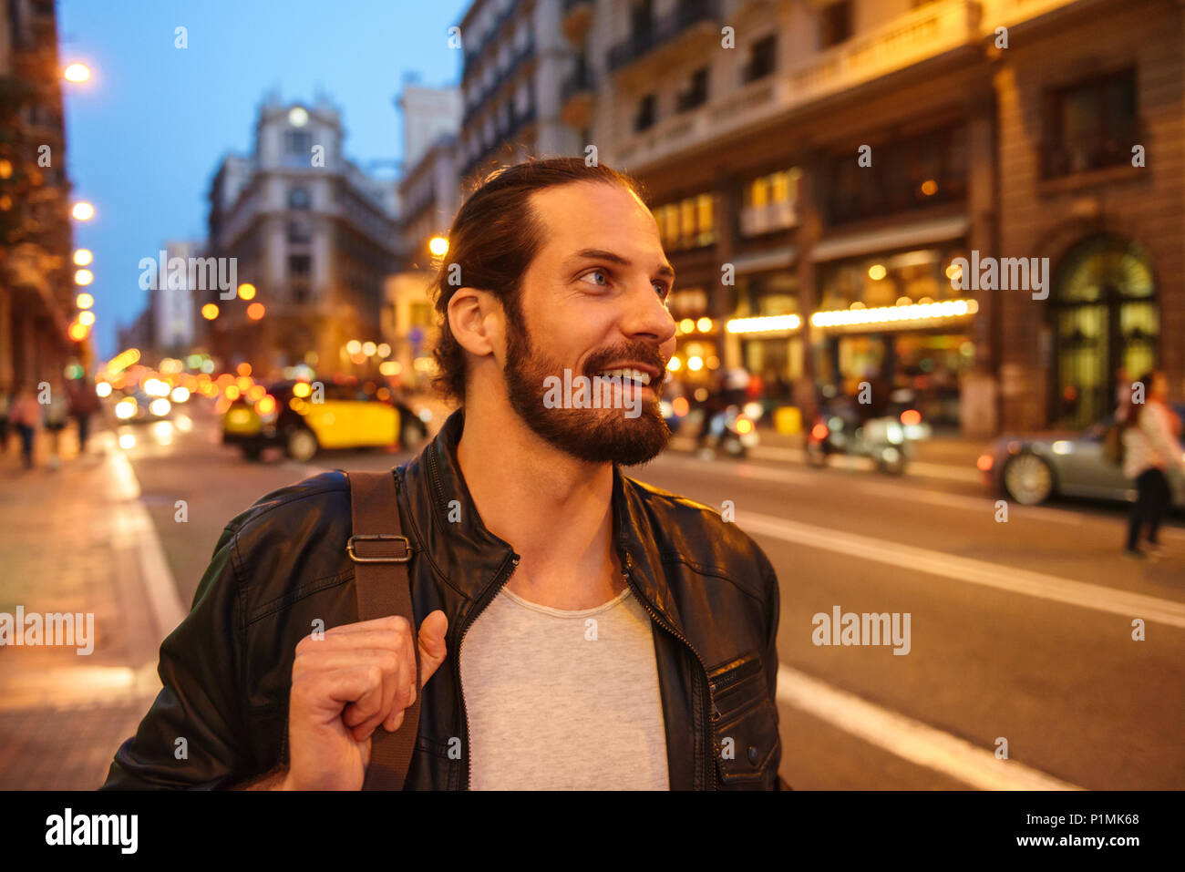 Portrait of smiling homme européen avec les cheveux attachés à la recherche de côté tout en marchant à travers megapolis en soir Banque D'Images