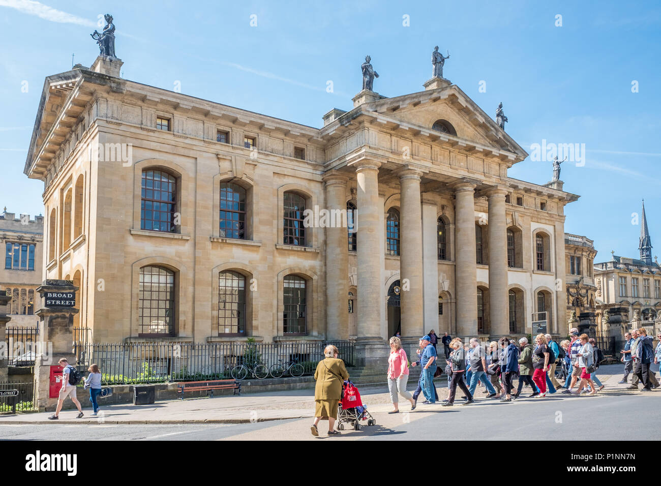 Un groupe de touristes à pied sur une large rue à Clarendon building de la Bodleian Library de l'université d'Oxford, en Angleterre. Banque D'Images