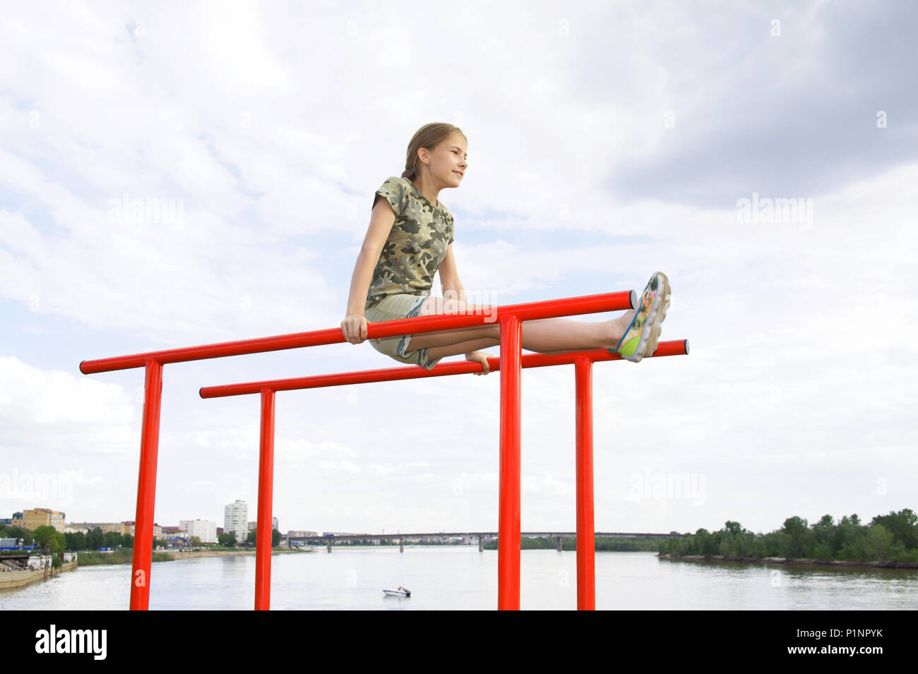 Athlétisme joyeux adolescente faisant une barre parallèle à profiter de l'extérieur. Dans l'arrière-plan, la rivière et le paysage urbain Banque D'Images