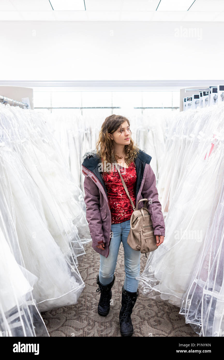 Young woman shopping for robe de mariage robes en boutique discount store allée, sac à main, de nombreux vêtements blancs pendaison de crémaillère sur ligne cintres Banque D'Images