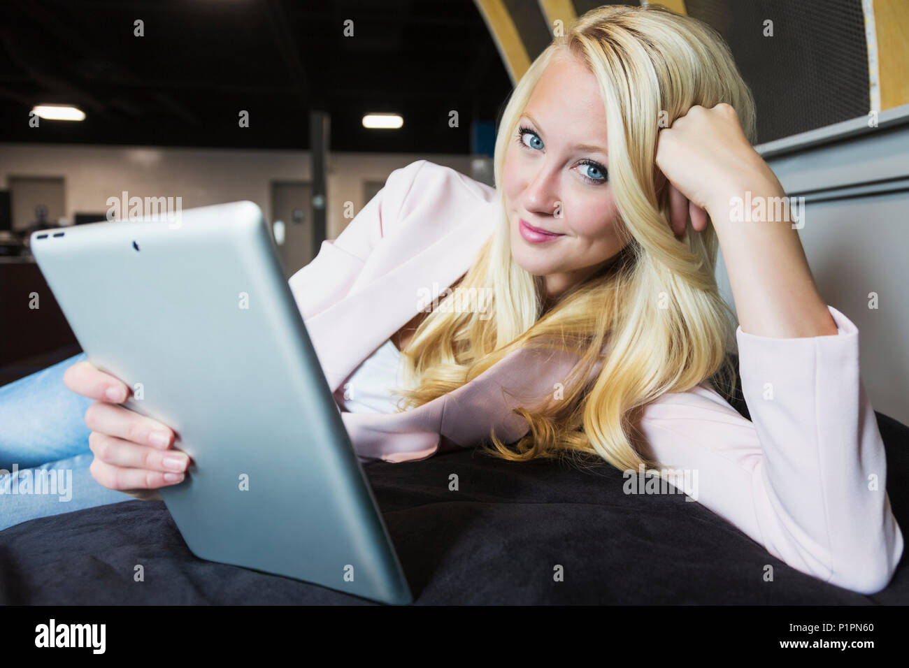 Portrait d'affaires d'une belle jeune femme d'affaires millénaire avec de longs cheveux blonds tenant une tablette dans une chaise de sac de beanbag et posant pour la caméra ... Banque D'Images