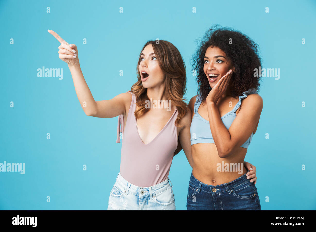 Deux jeunes filles enthousiastes habillés en vêtements d'été à pointage copie espace isolé sur fond bleu Banque D'Images