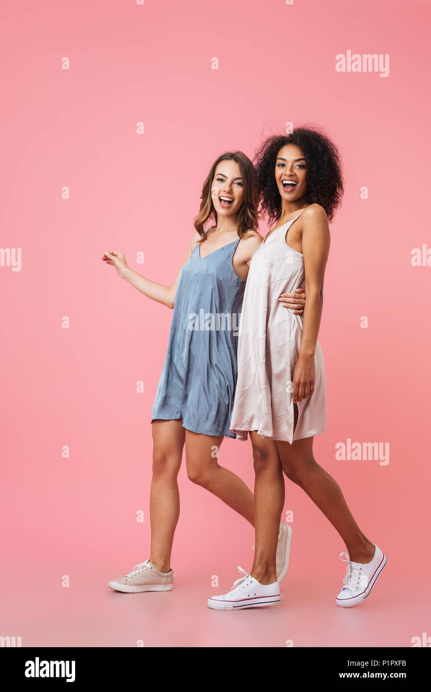Full Length portrait of smiling young deux filles habillés en vêtements d'été à s'éloigner et à la caméra au plus isolé sur fond rose Banque D'Images