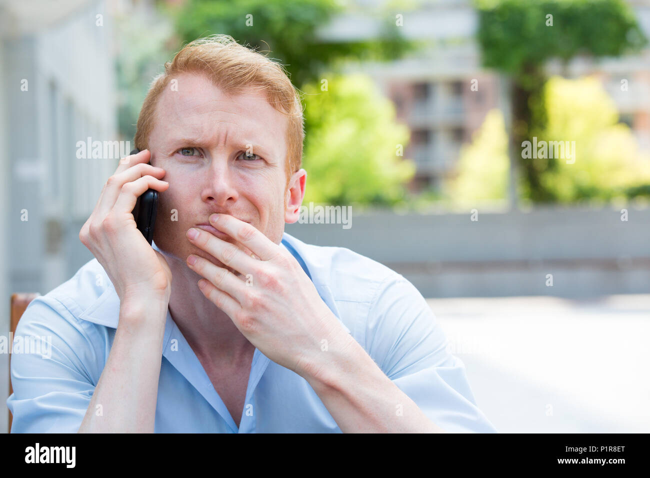 Closeup portrait, jeune homme perplexe, déconcerté, déconcerté, ahuri par quelqu'un parler sur son téléphone portable, isolé à l'extérieur contexte Banque D'Images