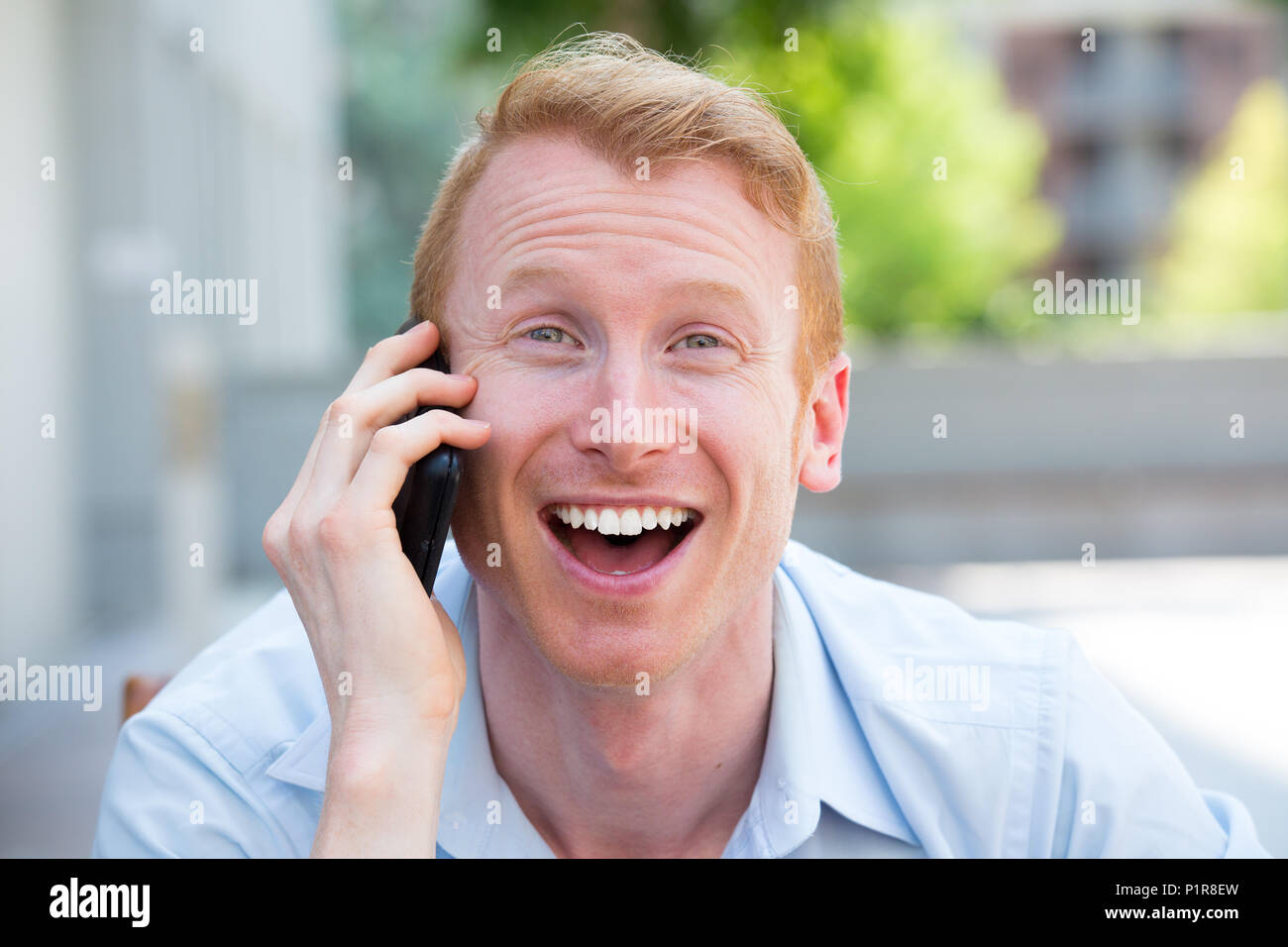 Closeup portrait, jeune homme extatique heureux avec bouche grande ouverte on cell phone, isolé à l'extérieur contexte Banque D'Images
