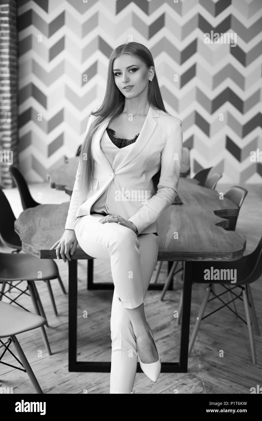 Belle jeune femme aux longs cheveux blonds tout droit en costume bleu assis à table en bois dans l'élégant intérieur moderne. La foudre naturelle Banque D'Images