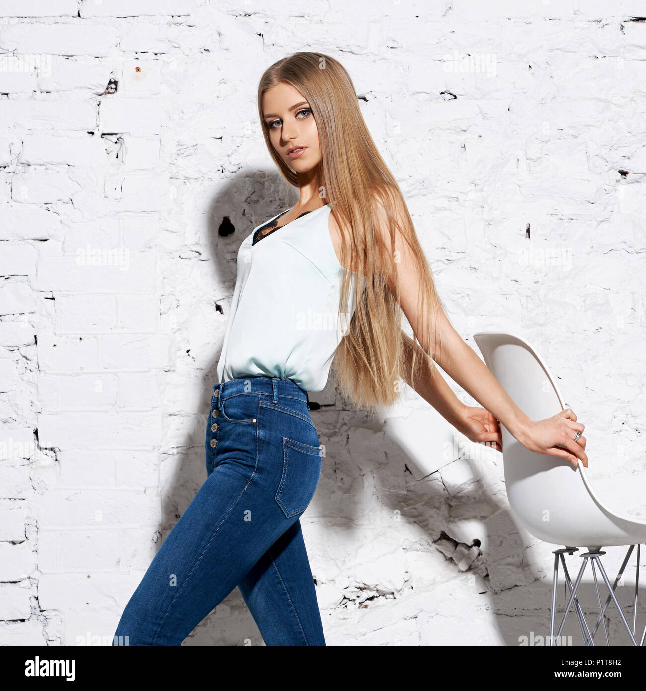 Belle jeune femme aux longs cheveux blonds tout droit en jeans et chemisier  blanc brillant permanent contre le mur de brique et posing Photo Stock -  Alamy
