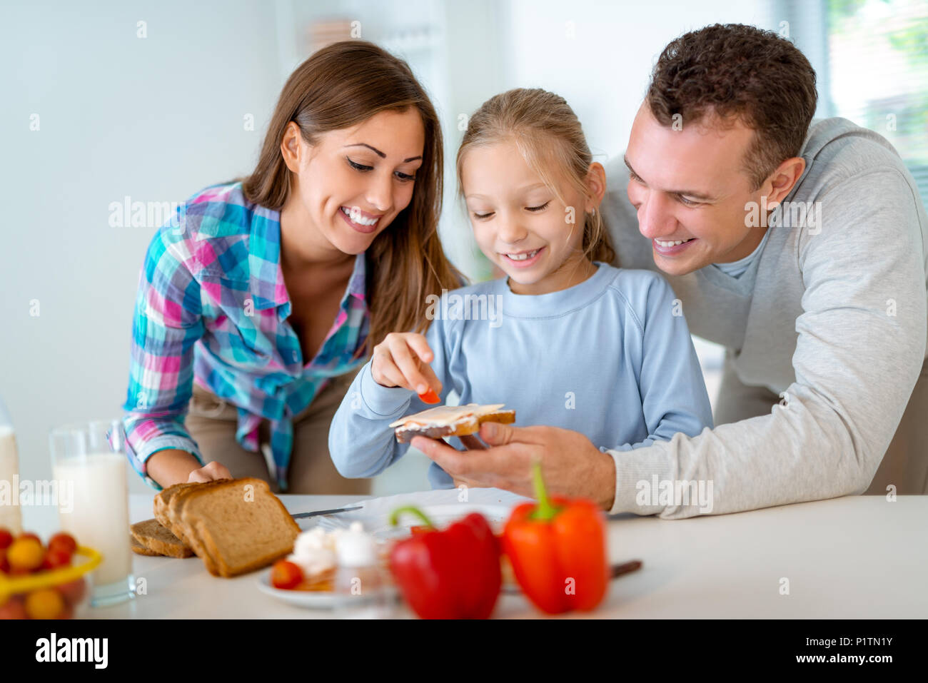 Beau jeune famille la préparation de repas sains pour le petit déjeuner dans la cuisine domestique. La mère apprend la petite fille comment faire un sandwich Banque D'Images