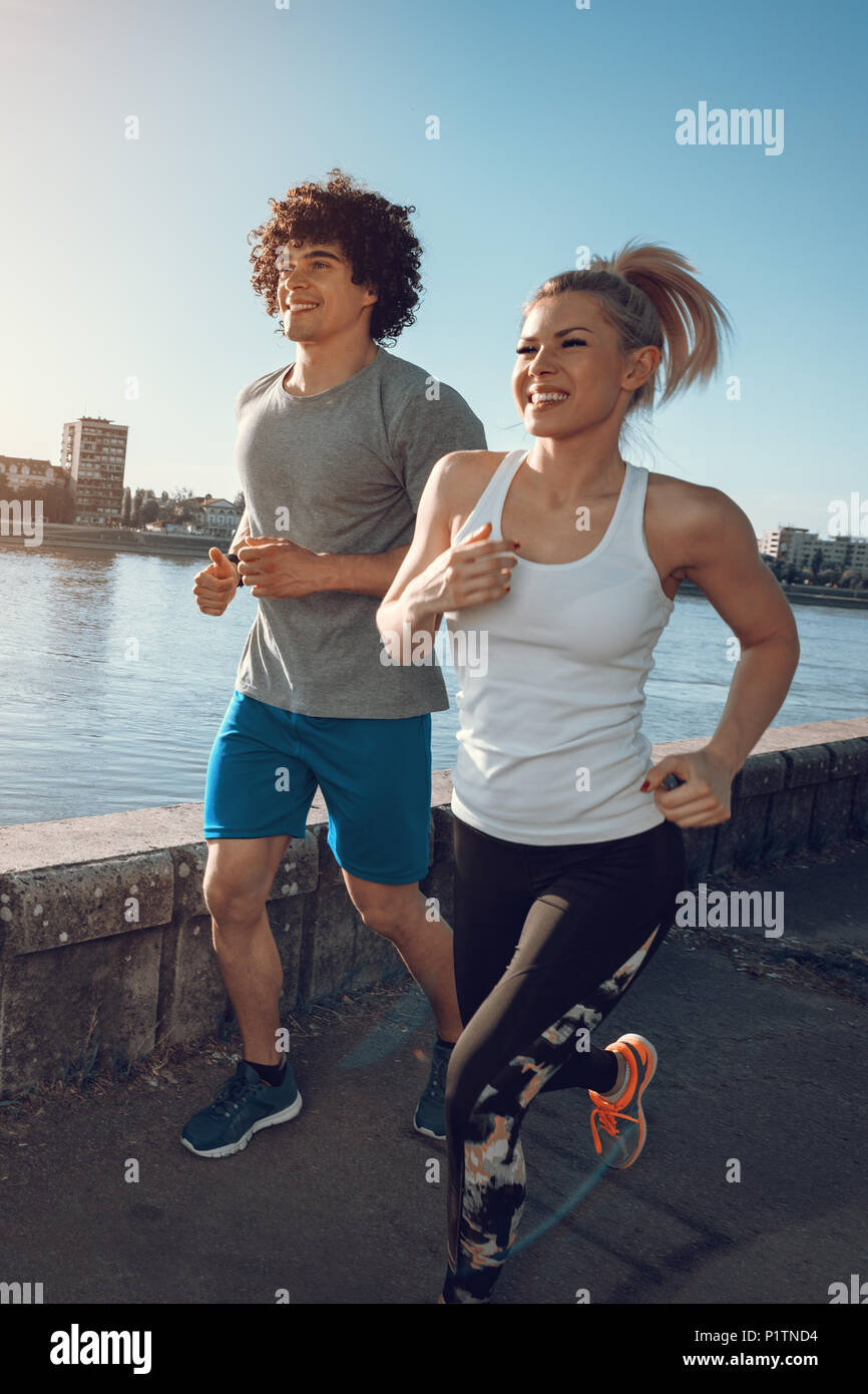 Les jeunes coureurs heureux couple extérieur formation par le fleuve, s'entraîner dans la nature contre ciel bleu avec le lever du soleil la lumière. Banque D'Images