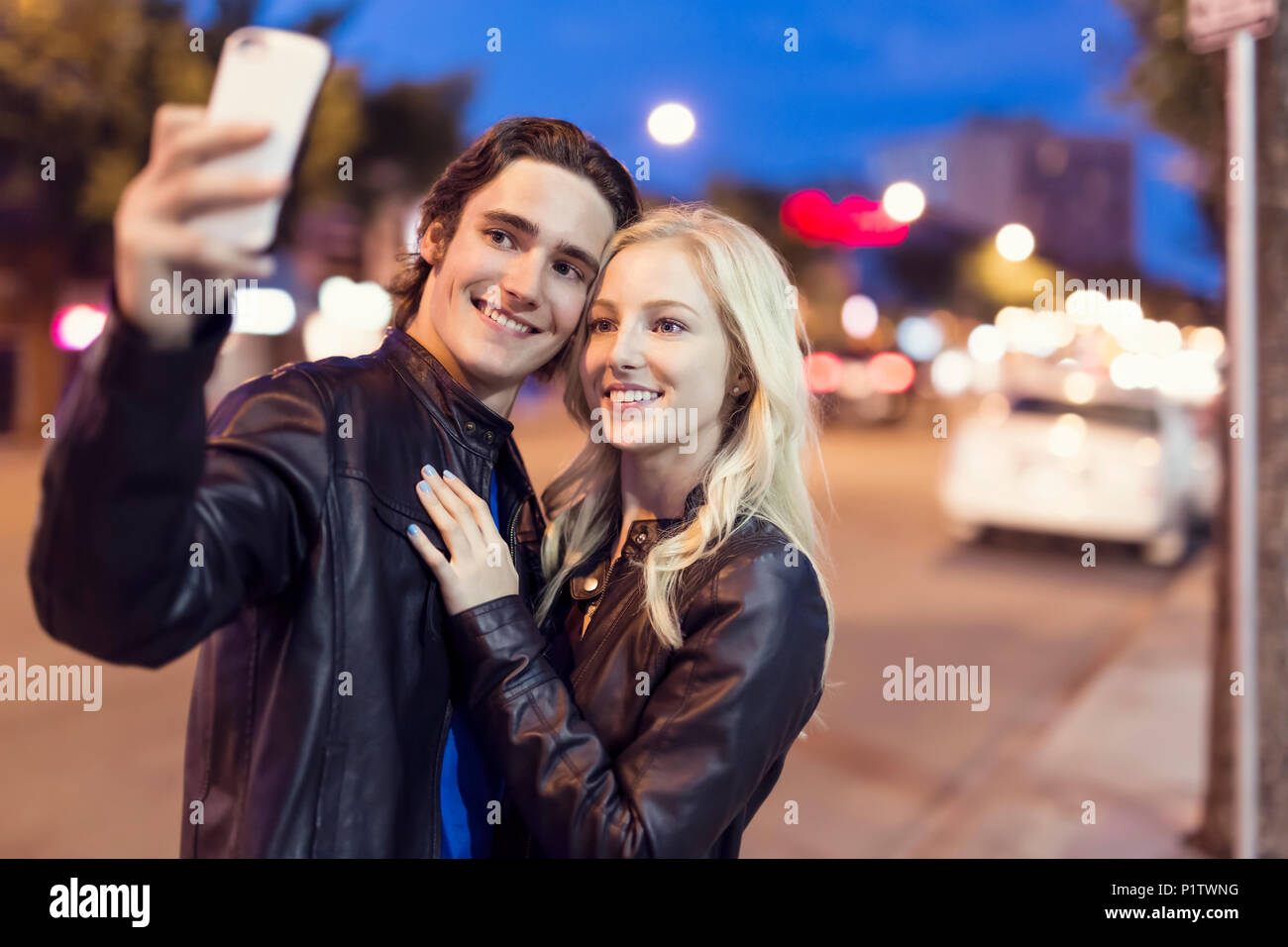 Un jeune couple faire un autoportrait avec un téléphone intelligent le long d'une rue au crépuscule ; Edmonton, Alberta, Canada Banque D'Images