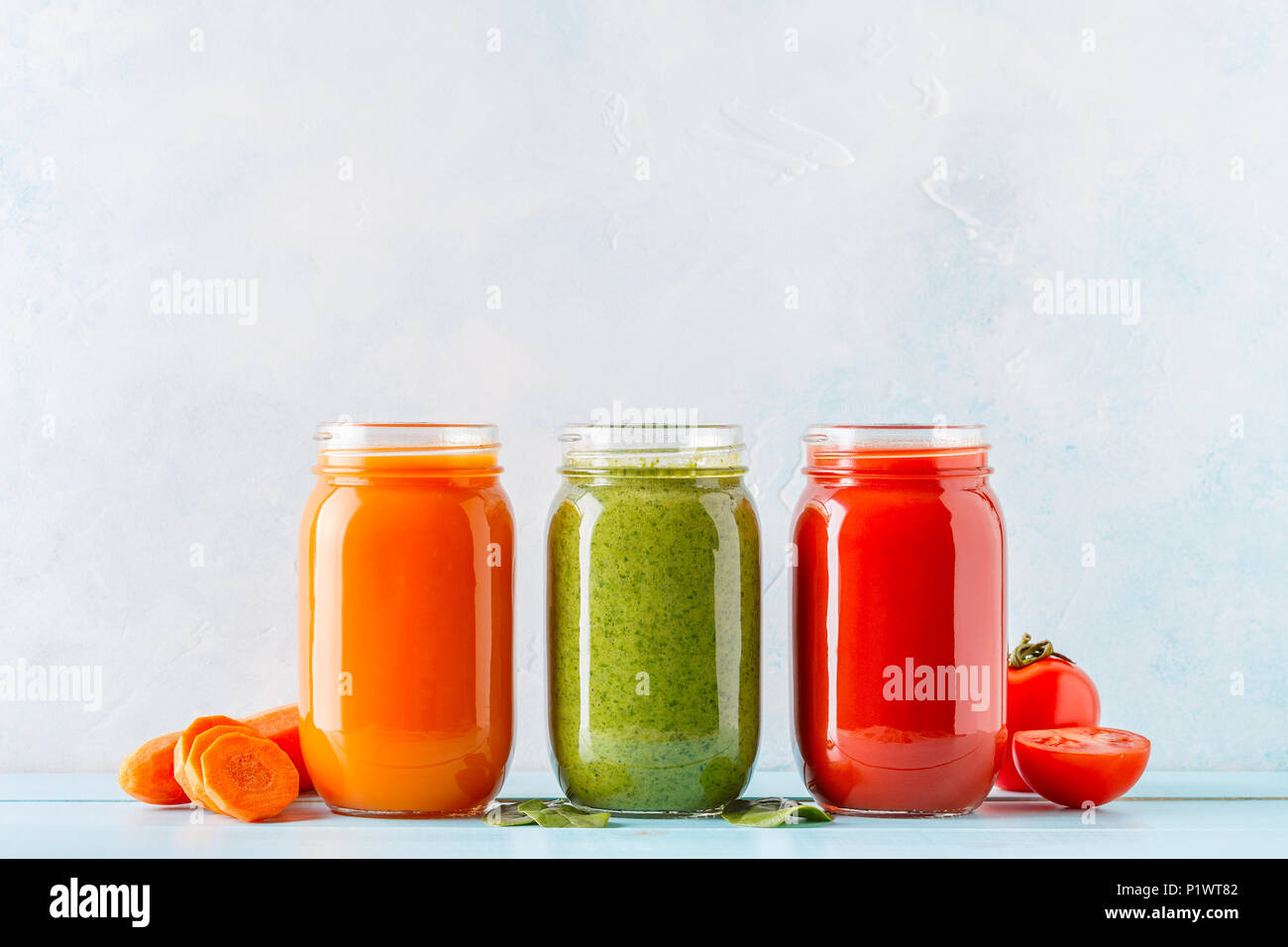 Orange/vert/rouge coloré / smoothies jus dans un pot sur un fond bleu. Banque D'Images