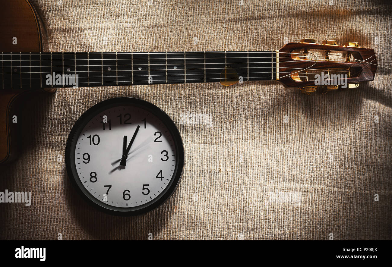 Composition simple, horloge murale noir sur lit couverture montrant douze heures et une partie d'un vieux rétro style tzigane, guitare acoustique. Banque D'Images