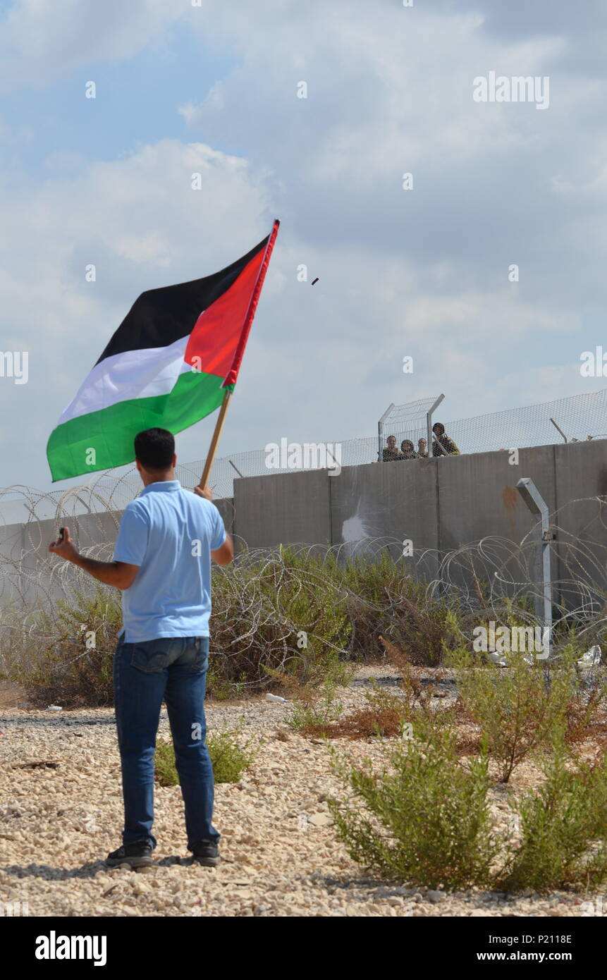 18 septembre 2014 - Bil'in, Ramallah et al-Bireh Governora, Israël - l'armée israélienne lance une grenade de gaz lacrymogène sur les manifestants alors qu'un homme avec un drapeau montres lors de la manifestations Vendredi.Bilin est un village de Palestine qui proteste régulièrement la construction de la proximité des colonies israéliennes. La population palestinienne locale pense que les colonies israéliennes sont illégales et sont des terres d'occupation ancienne propriété de familles palestiniennes vivant dans le village. Crédit : Edward Crowford SOPA/Images/ZUMA/Alamy Fil Live News Banque D'Images