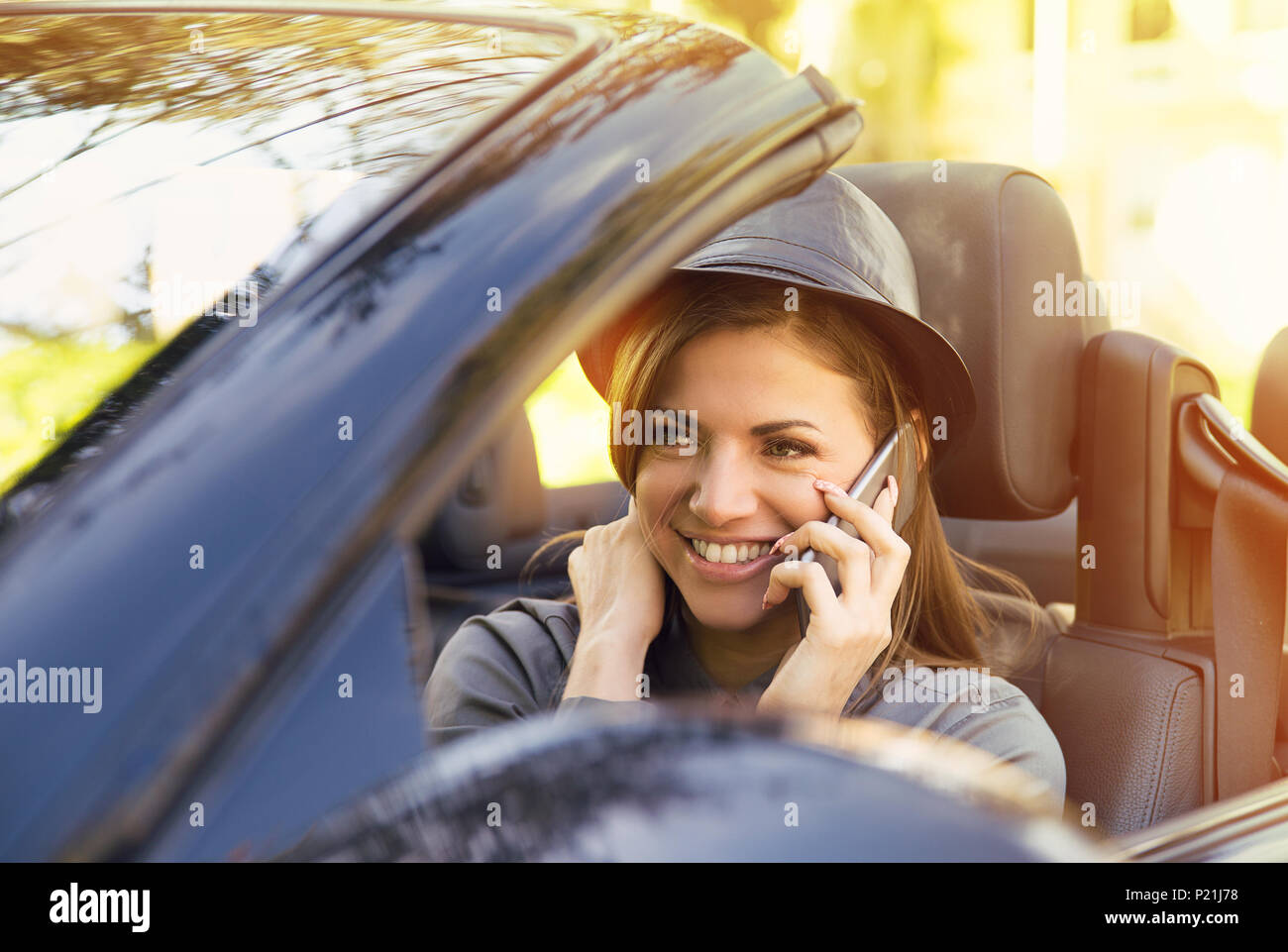Happy cute femme assise dans sa nouvelle voiture décapotable talking on mobile phone on a sunny day Banque D'Images