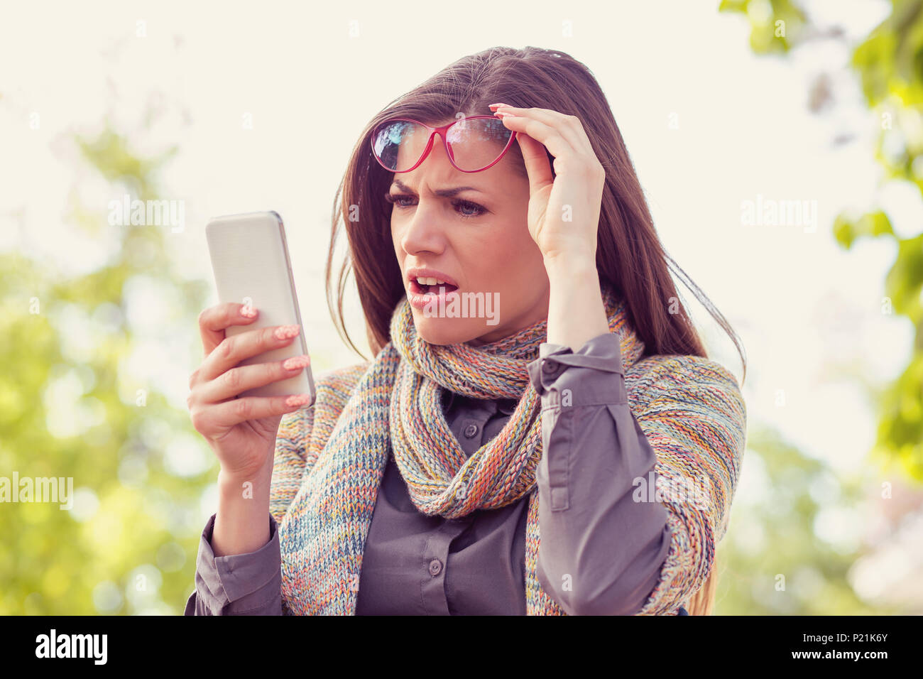 Femme en colère Ennuyé à lunettes à son téléphone intelligent avec frustration en marchant sur une rue sur une journée d'automne Banque D'Images