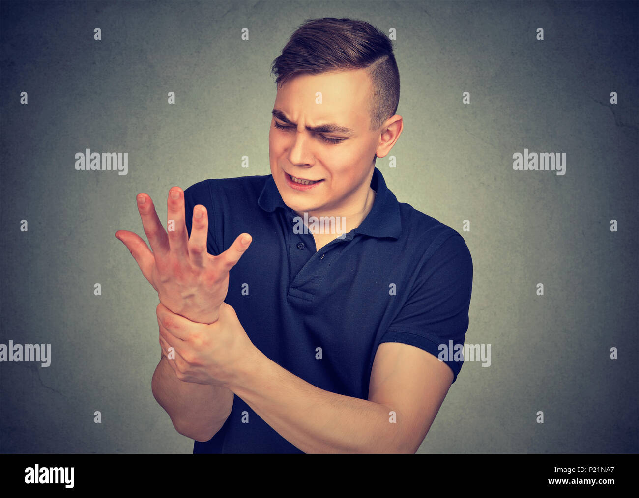 Jeune homme tenant son poignet douloureux isolé sur fond de mur gris. Douleur d'entorse Banque D'Images