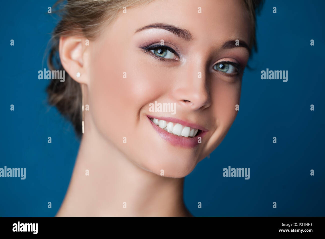Young smiling woman face sur fond bleu, closeup portrait. Sourire mignon Banque D'Images