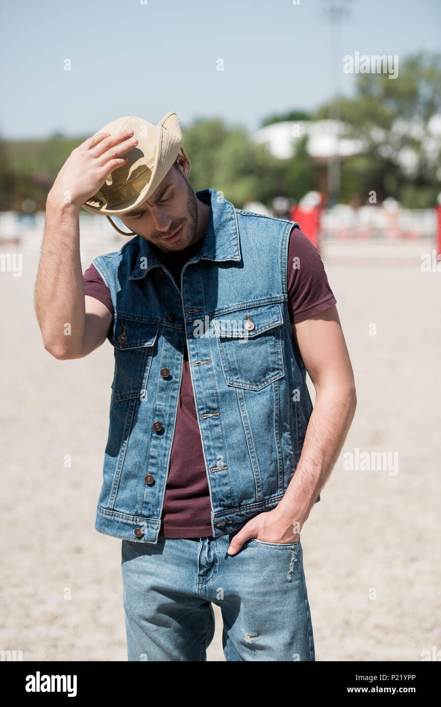 Young man wearing cowboy hat et denim vest debout sur ranch Banque D'Images