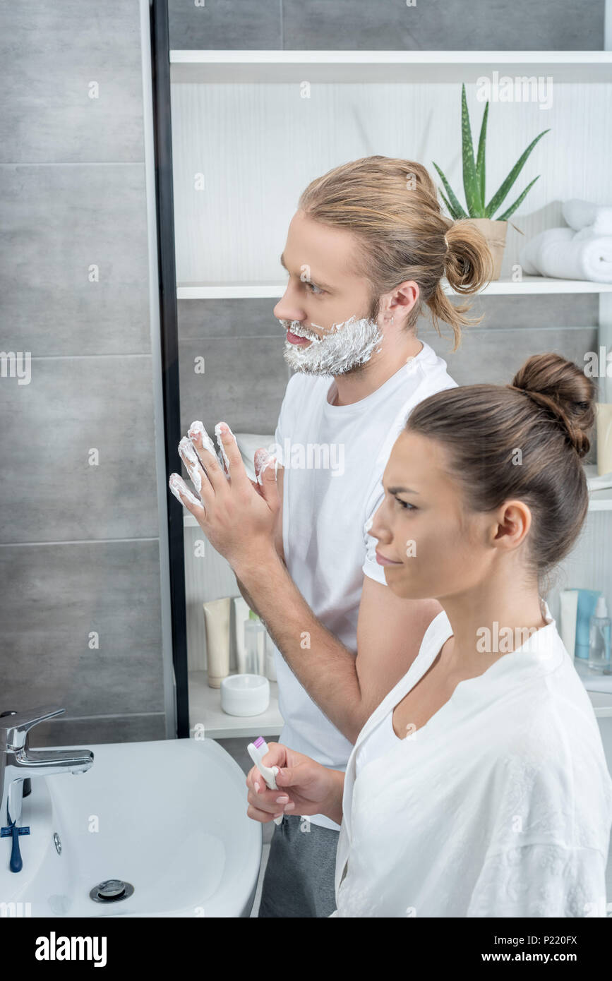 Rasage homme femme tandis que sa barbe se brosser les dents dans la salle de bain le matin Banque D'Images