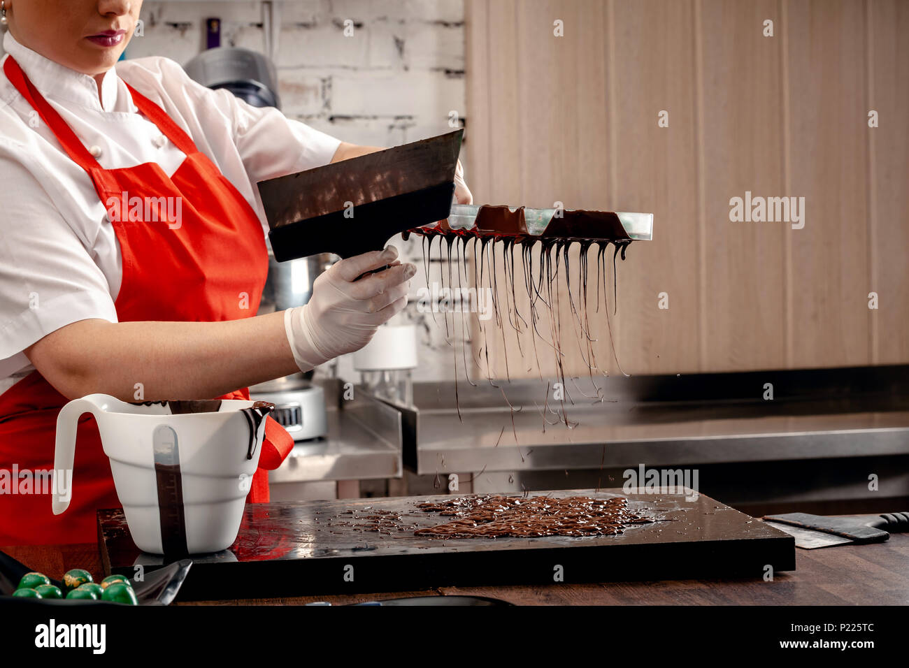 Une femme pâtissier avec uniforme rouge et blanc des gants stériles n un ensemble de chocolats colorés de chocolat au lait sur une table. Banque D'Images
