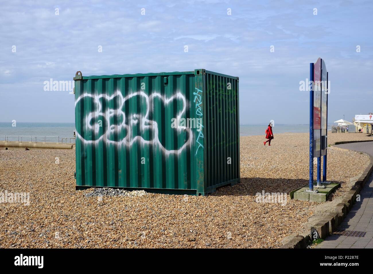 Vert de mer contenant avec graffiti blanc sur une plage avec un mystère femme en rouge dans l'arrière-plan Banque D'Images