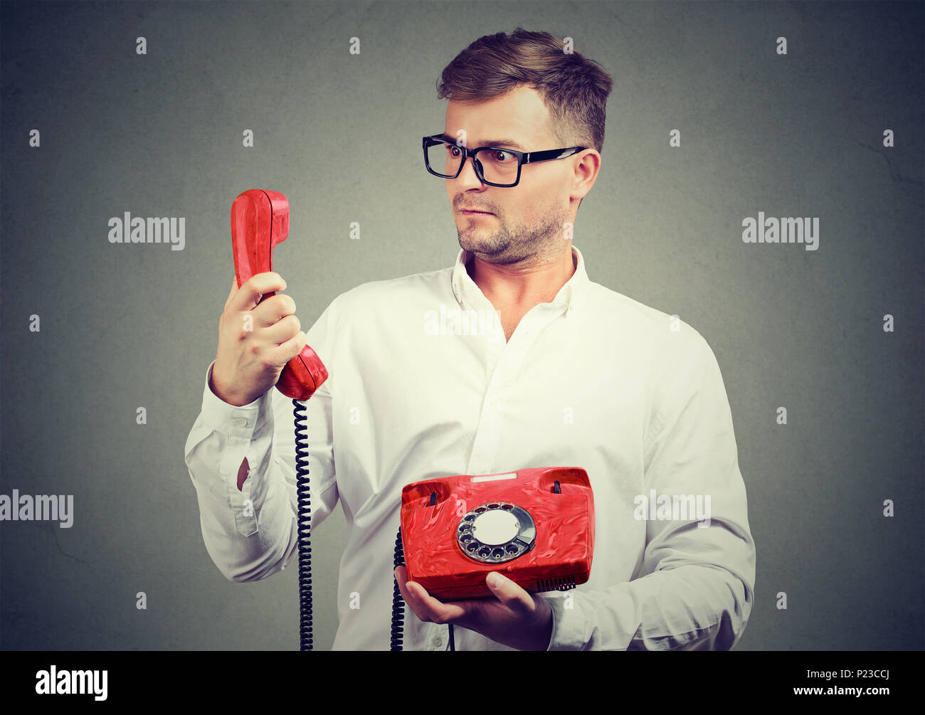 Jeune homme à lunettes holding red vieux téléphone à le regarder en grand étonnement. Banque D'Images
