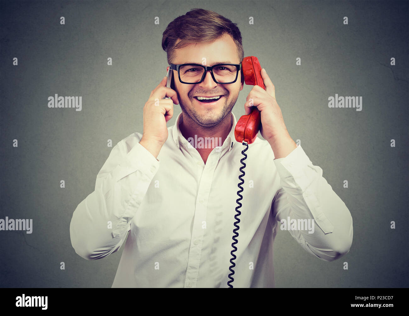 Beau jeune homme parlant à la fois sur le téléphone rouge à l'ancienne et nouveau smartphone étant occupé. Banque D'Images