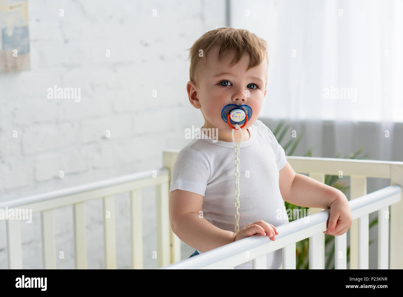 Cute little baby boy avec sucette dans lit bébé looking at camera at home Banque D'Images