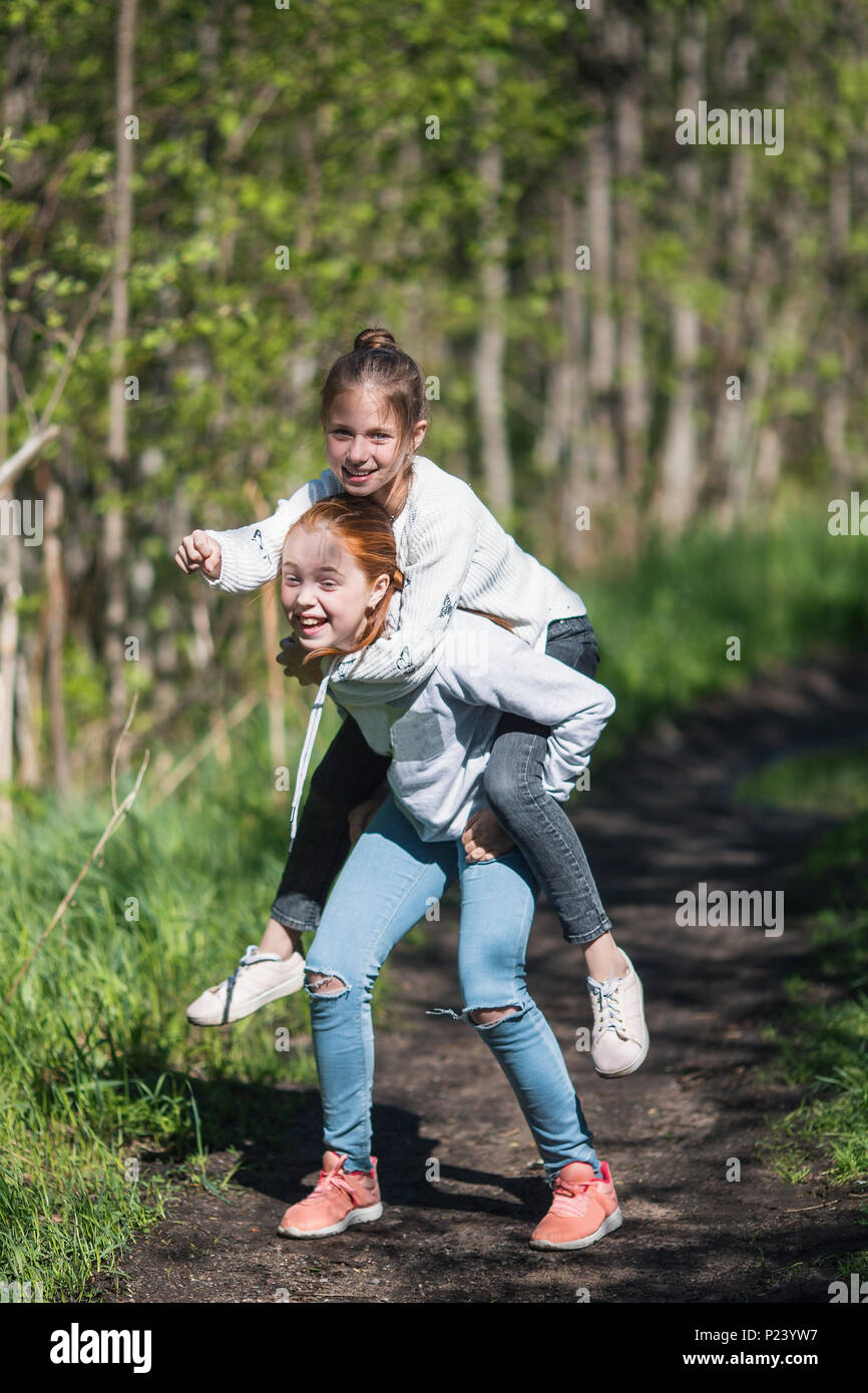 Deux soeurs filles adolescents amis équitation les uns les autres s'amuser dans le parc à l'été. Banque D'Images