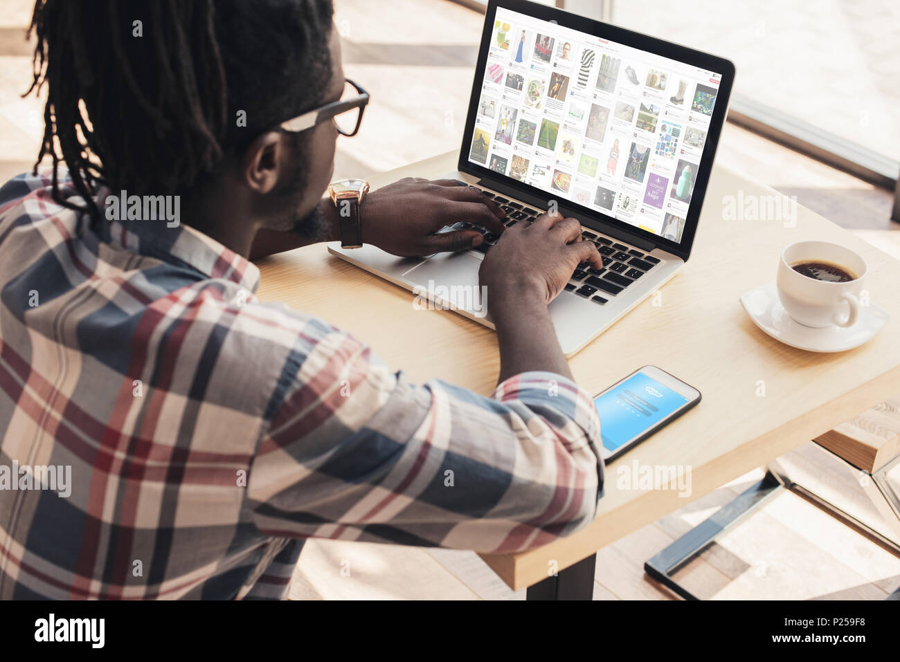 African American man using laptop avec pinterest site web et smartphone avec appareil skype Banque D'Images
