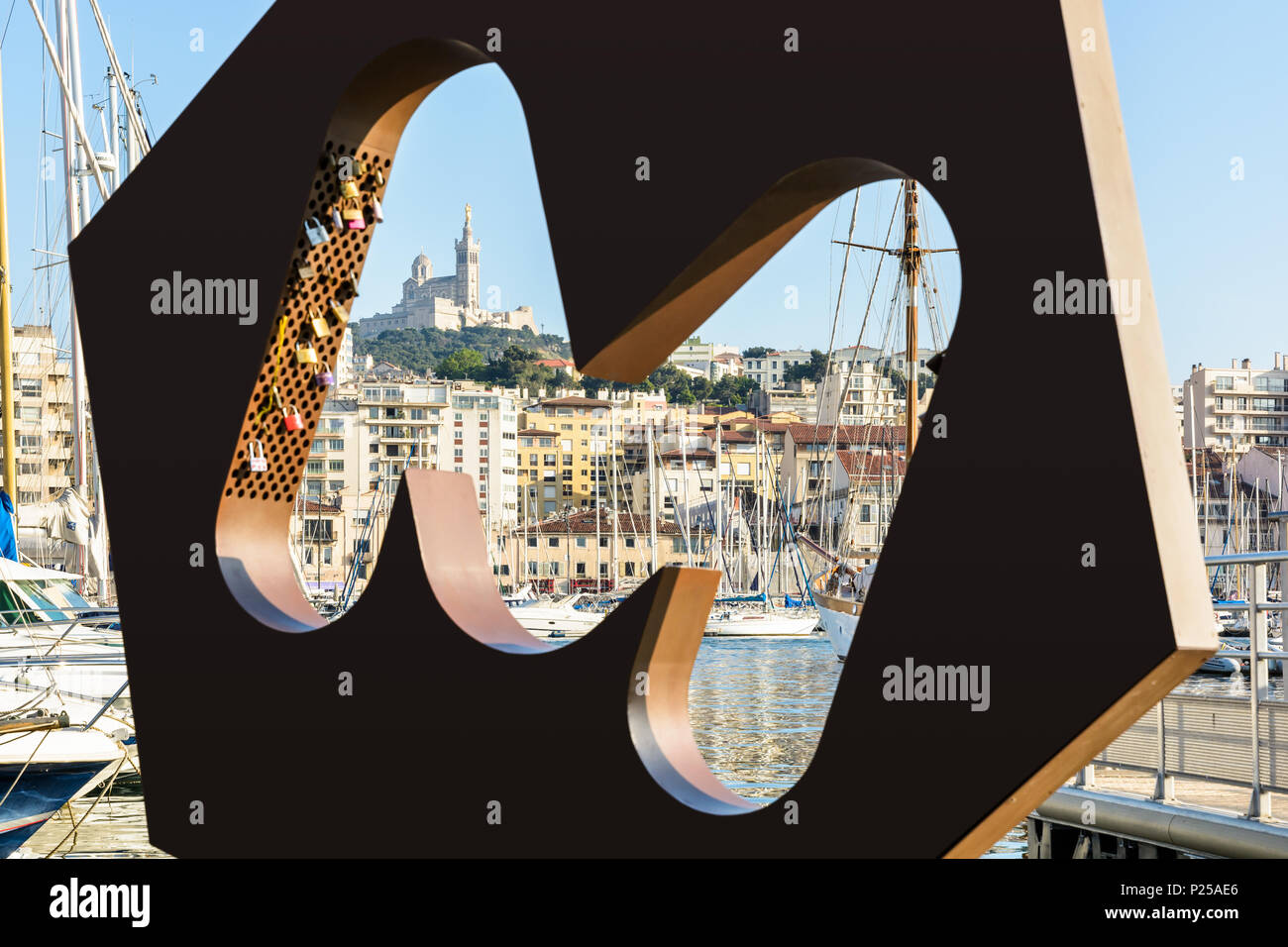 La Basilique de Notre-Dame de la Garde vue depuis le Vieux Port via le logo M de la ville de Marseille, avec l'amour d'isolation et de bateaux dans la marina. Banque D'Images