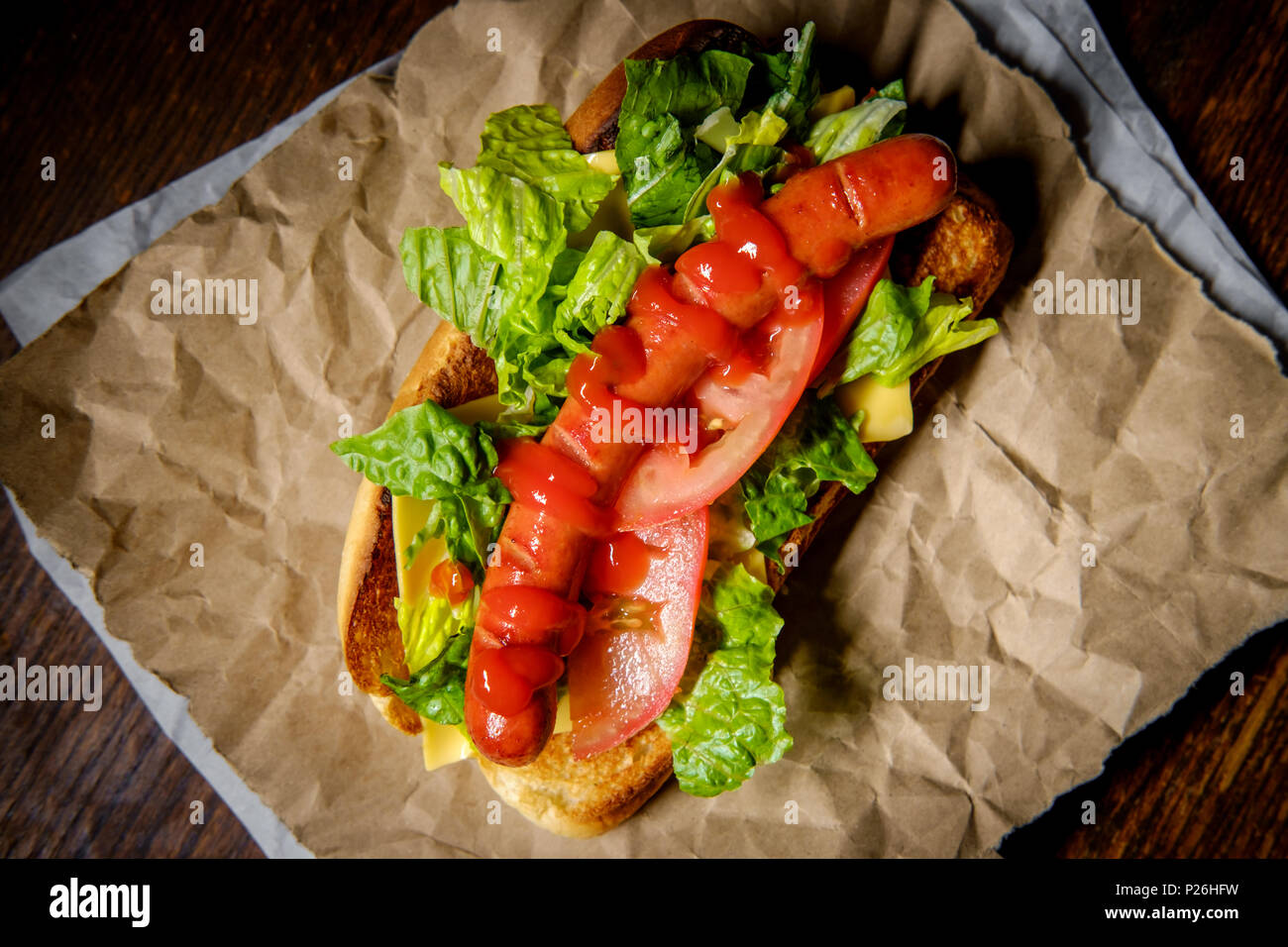 Hot-dog grillé fantaisie avec laitue tomate fromage américain et ketchup Banque D'Images