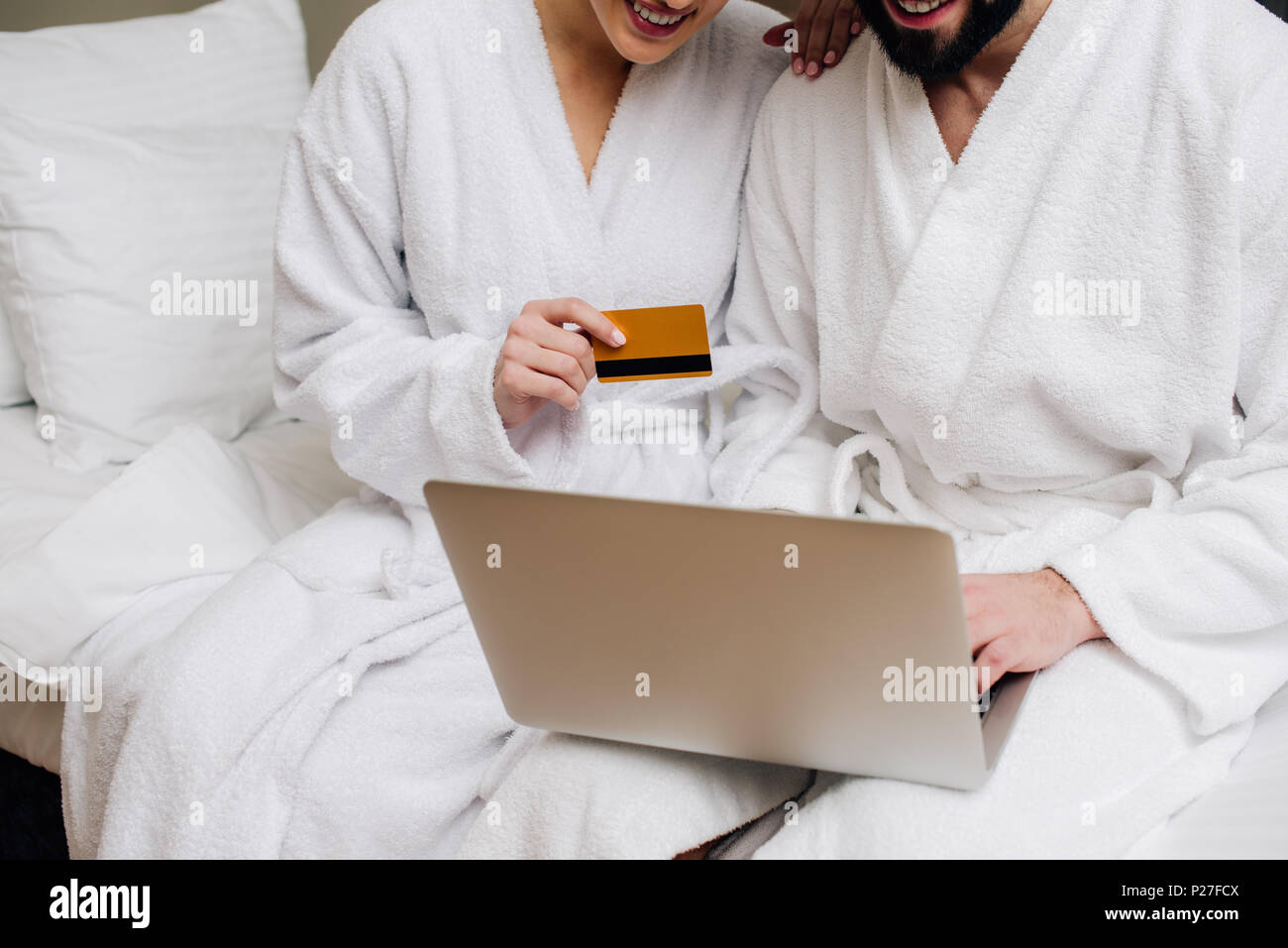 Cropped shot of couple en peignoirs faire e-boutique avec ordinateur portable et carte de crédit à l'hôtel suite Banque D'Images