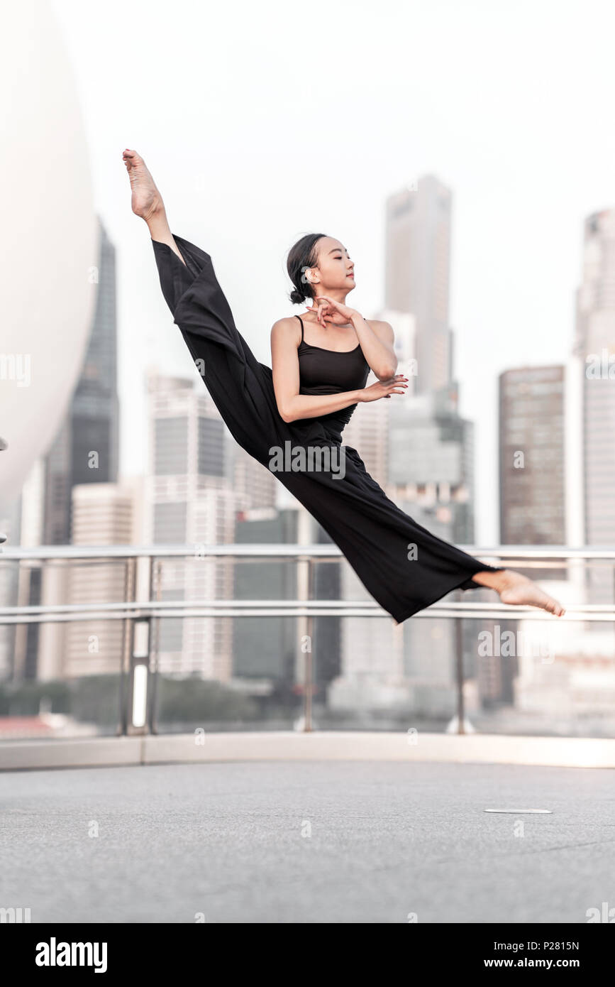Belle jeune fille dansant dans la ville, vêtu de noir, avec des gratte-ciel en arrière-plan Banque D'Images