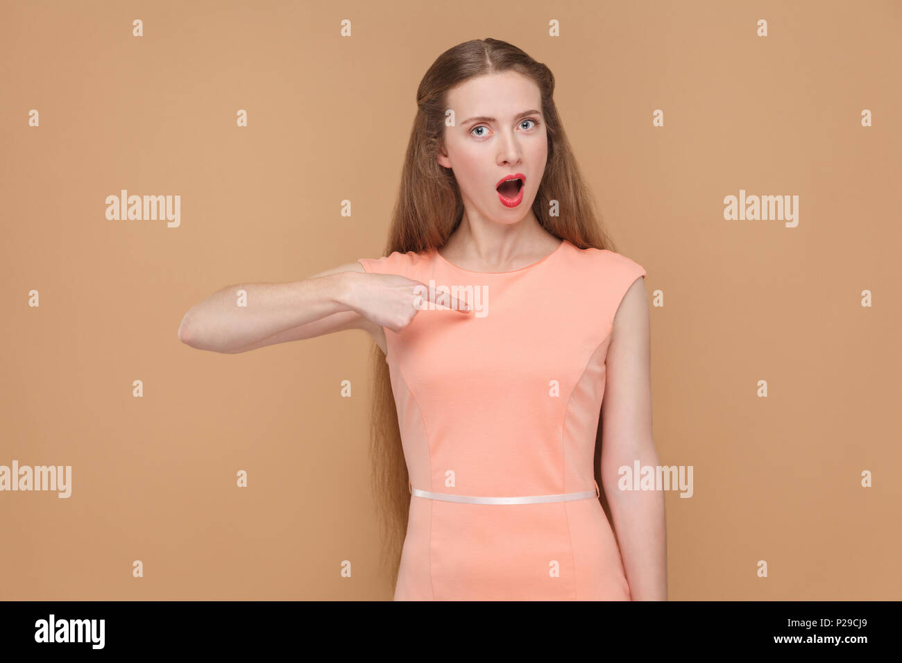 C'est que moi ? Surprised woman looking at camera. portrait d'une jolie, belle femme aux longs cheveux et maquillage en robe rose. , Studio shot, iso Banque D'Images