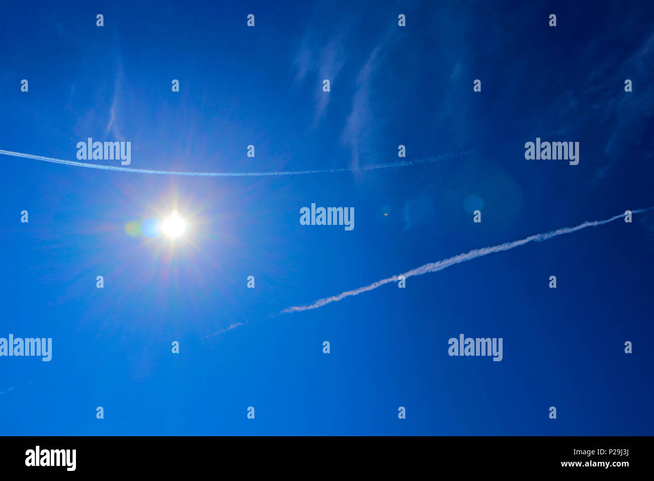 Grand soleil à l'aide de fusées éclairantes et auréole spectrale autour de contre ciel bleu avec des traces de jet blanc Banque D'Images