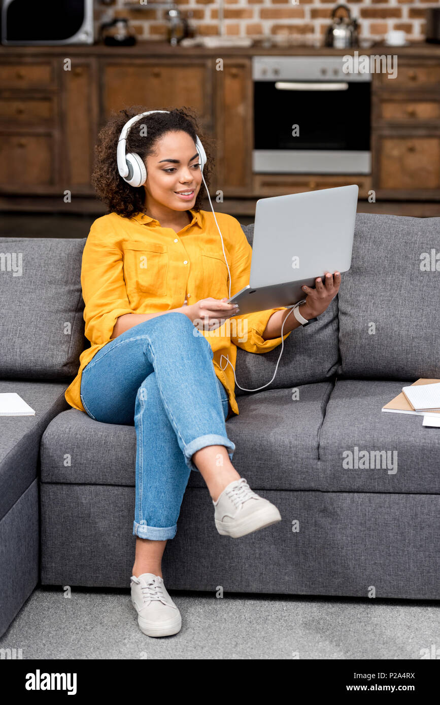 Souriante jeune femme travaillant avec un ordinateur portable et d'écouter la musique à la maison Banque D'Images