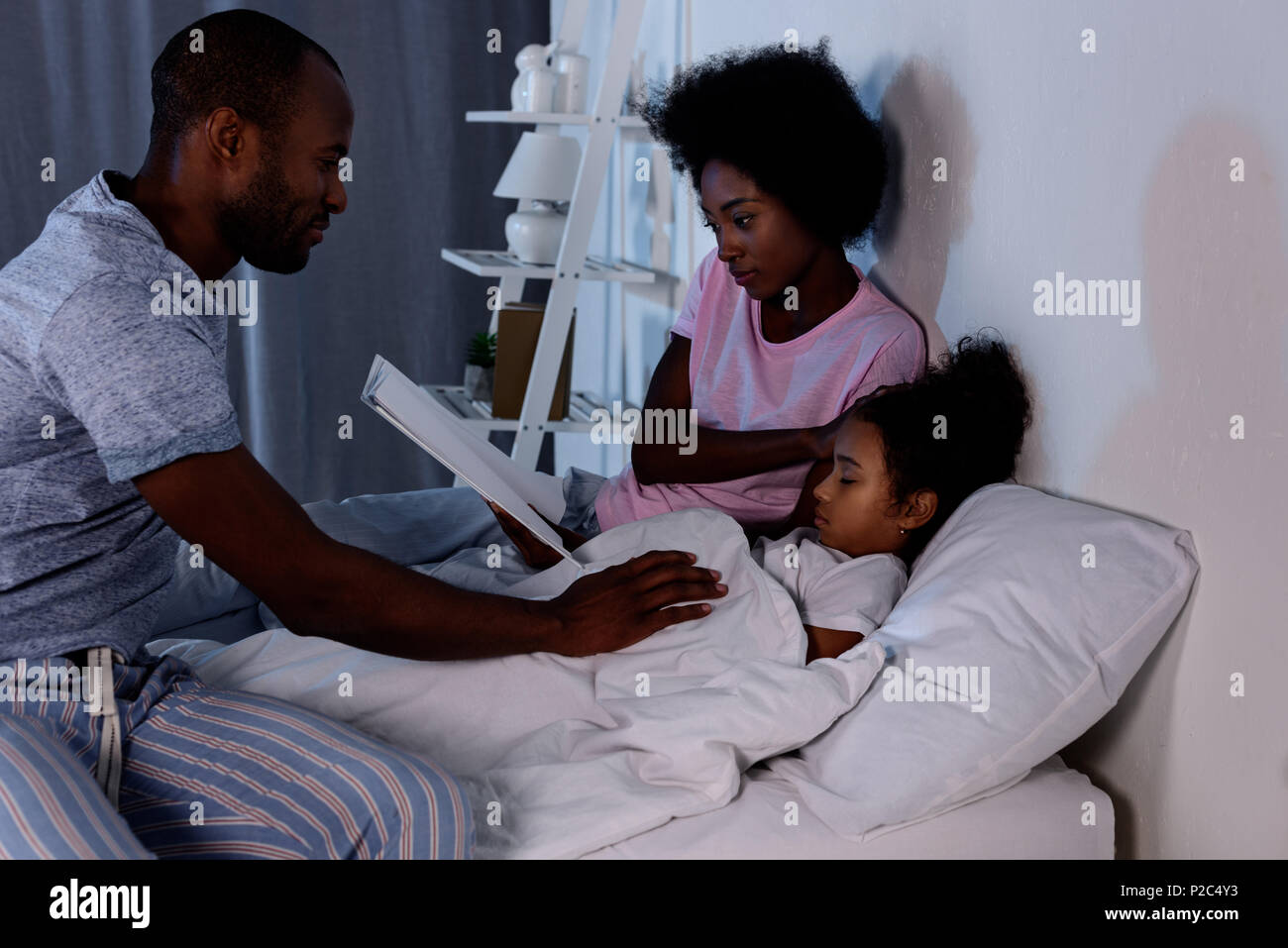 African American parents lecture fille avant de dormir à la maison Banque D'Images