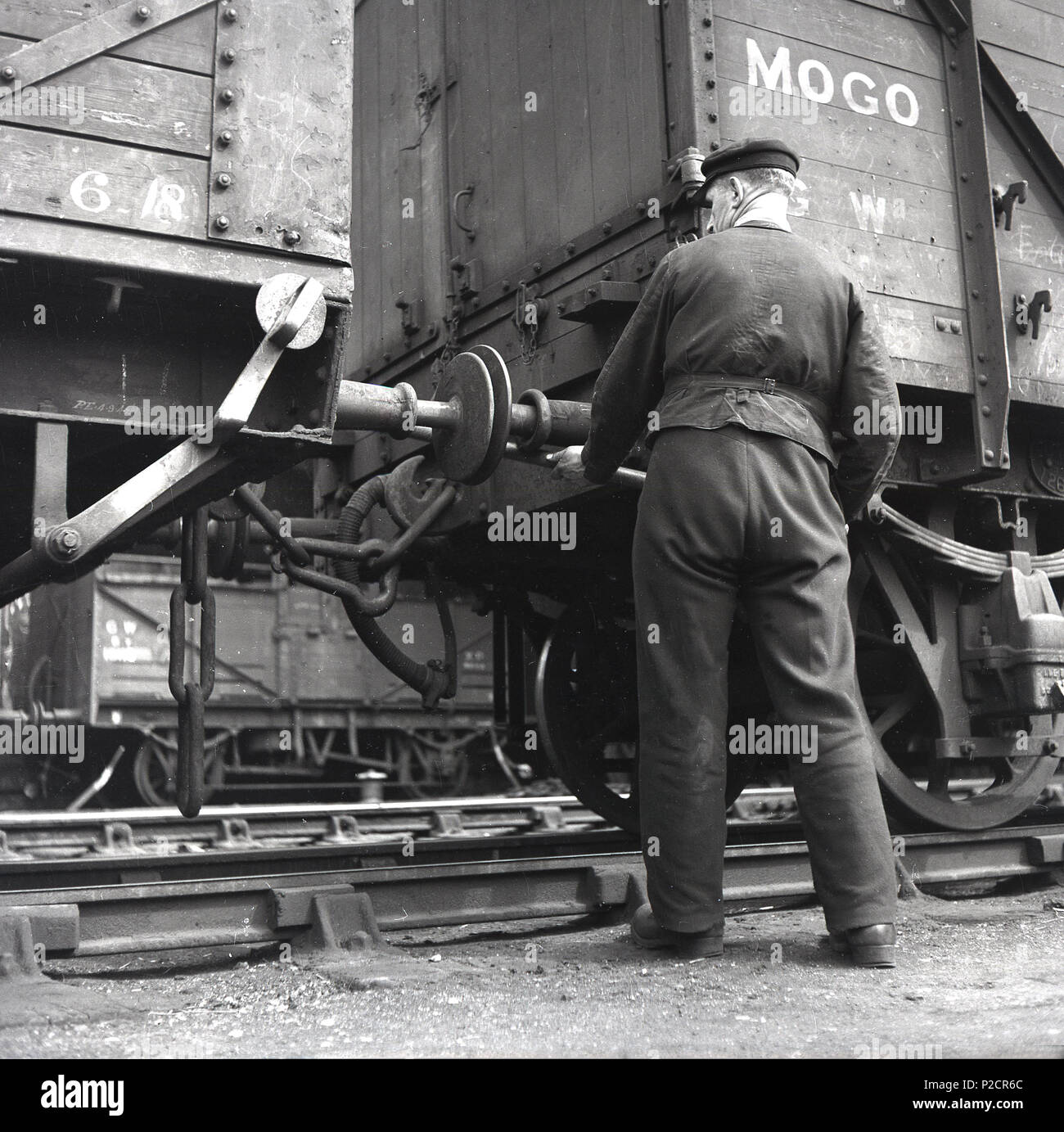 Années 1950, historique, un employé des chemins de fer, à côté d'une sellerie, d'une locomotive ferroviaire qui lie deux grands pans de bois les wagons de fret, England, UK. Son travail manuel, mais de manoeuvre ferroviaire jouent un rôle important dans l'industrie ferroviaire, dans les secteurs commercial et de marchandises. Banque D'Images